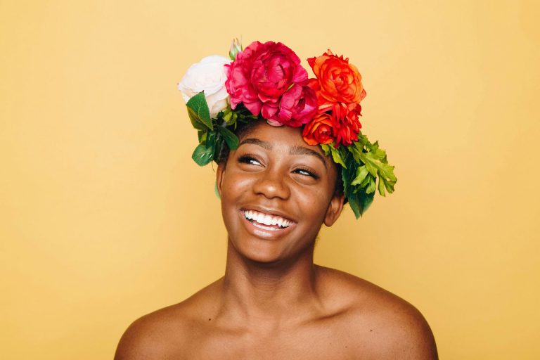 Smiling young Black woman wearing a colourful flower crown against a yellow background